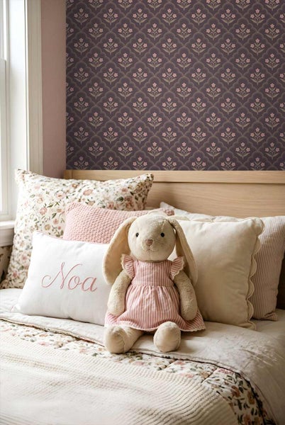 Schlafzimmer mit geblümter Tapete in einem Bogenmuster. Auf dem Bett liegen verschiedene Kissen und ein Stoffhase.