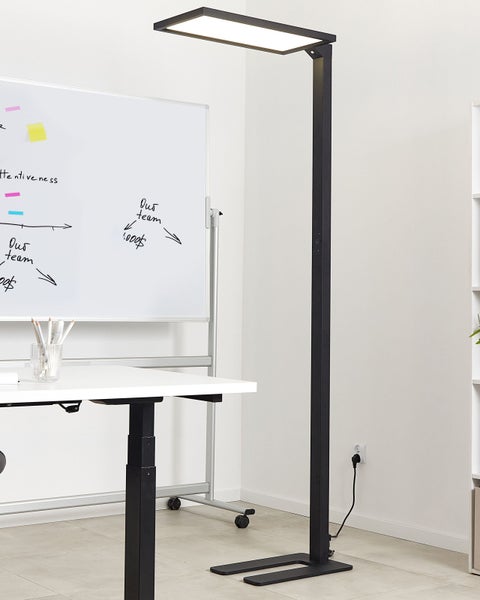 Moderne Stehleuchte aus Metall neben einem Schreibtisch und Whiteboard für Büroumgebungen.