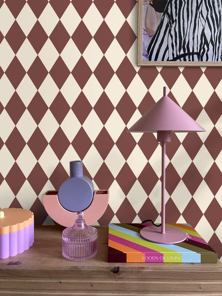 Szene mit Rautenmuster-Tapete, Tischleuchte und dekorativen Objekten auf einem Tisch