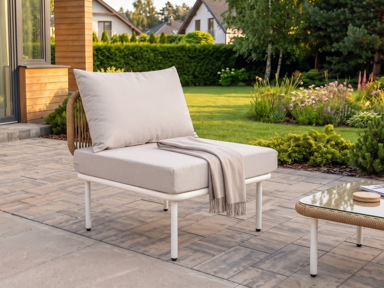 Moderner Garten-Loungesessel mit dicken Polstern und Seilgeflecht-Rückenlehne auf einer gepflasterten Terrasse vor einem grünen Garten.