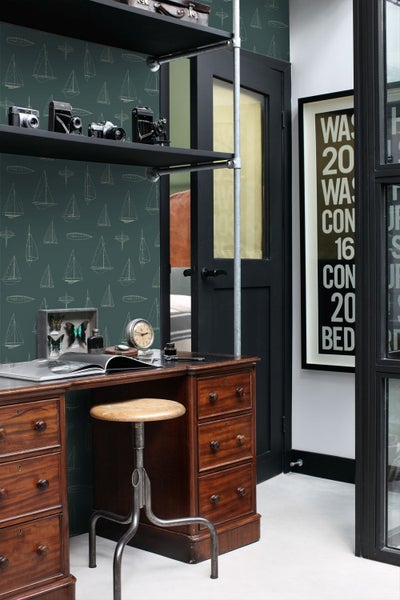 Arbeitszimmer im Vintage-Stil mit dunkelgrüner Vliestapete mit weißen Segelboot-Skizzen, klassischem Holzschreibtisch und Industrieregalen.