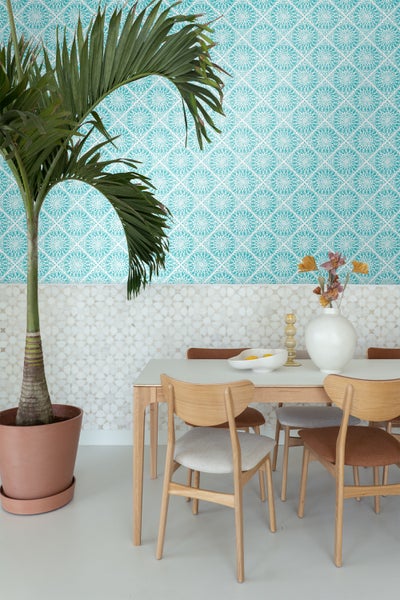 Esszimmer mit Esstisch, Stühlen und Zimmerpflanze vor gemusterter Tapete.