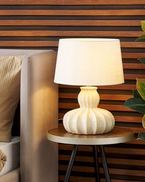 Dekorative Tischlampe mit Stoffschirm auf einem Beistelltisch neben einem Bett