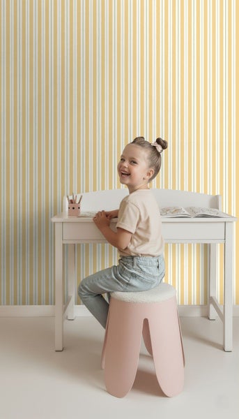 Mädchen sitzt an einem weißen Schreibtisch vor einer gestreiften Tapete