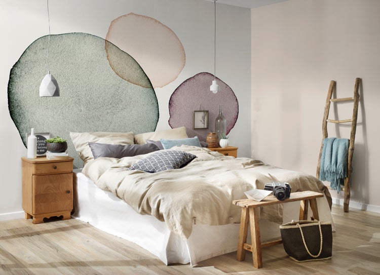Hell eingerichtetes Schlafzimmer mit Doppelbett, Fototapete mit Kreis-Motiven, Holznachtisch, Holzbank und einer dekorativen Leiter.