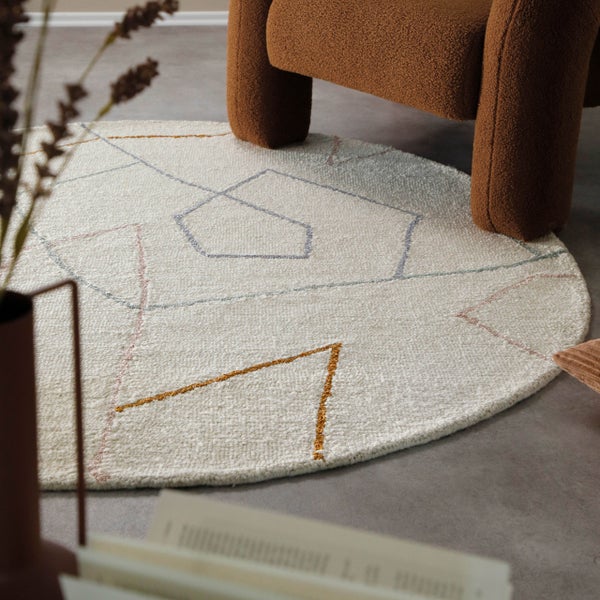 Runder Teppich mit geometrischem Linienmuster in einem modern eingerichteten Wohnzimmer neben einem Sessel.