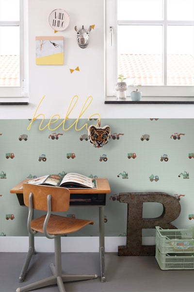 Vliestapete mit Motiven von Baustellenfahrzeugen wie Traktoren und Baggern in einem hellen Kinderzimmer mit Schreibtisch und Dekoration.