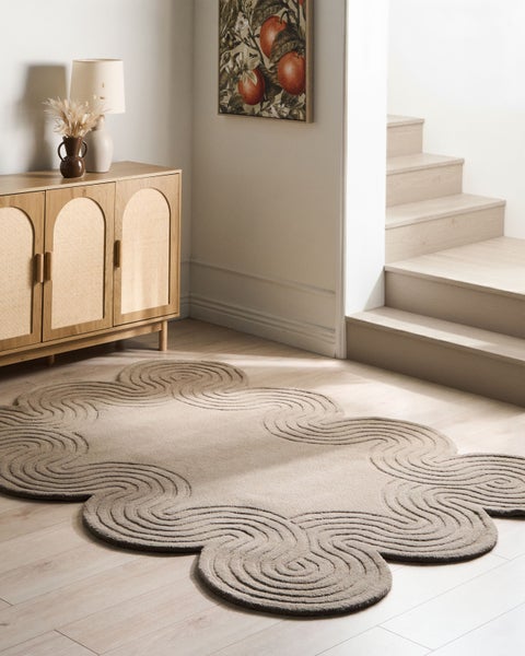 Beige Teppich mit Wellenrand und Spiralmuster in einem hellen Raum neben einem Sideboard aus Holz und einer Treppe.