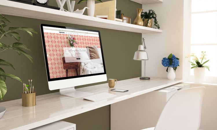 Moderner Arbeitsplatz mit weißem Schreibtisch, Computermonitor mit Tapetenshop-Website, Regalen und Zimmerpflanzen vor einer olivgrünen Wand.