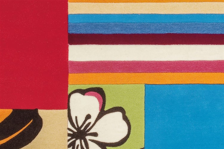 Nahaufnahme eines Teppichs mit buntem Muster aus Streifen, Farbblöcken und einem Blumenmotiv.