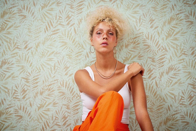 Frau posiert vor einer floral gemusterten Tapete.