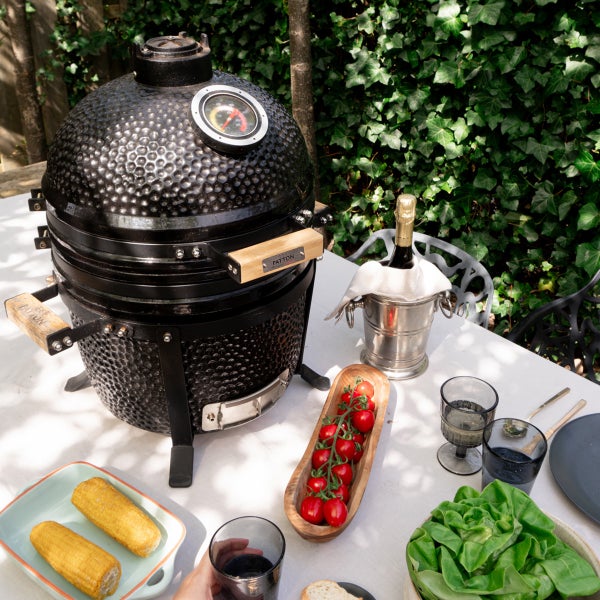 Keramikgrill auf einem Tisch mit Speisen im Garten