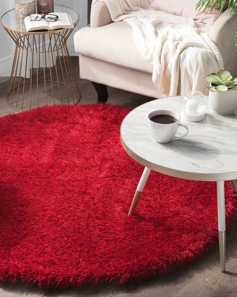 Runder, roter Hochflor-Teppich in einem hellen Wohnzimmer mit Sessel und Marmortisch auf Holzboden.