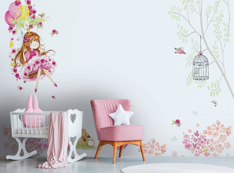 Helle Kinderzimmer-Einrichtung mit Fototapete mit schaukelndem Mädchen, Bäumen und Blumen. Mit Wiege aus Holz und Polstersessel.