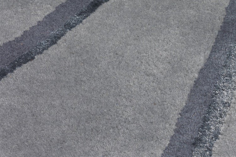 Detailaufnahme eines weichen Teppichs mit grauem Wellenmuster und dunklen Streifen.