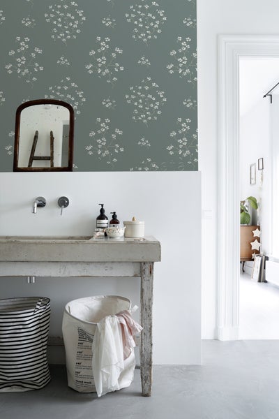Badezimmer mit Waschbecken, Spiegel und Wäschekörben vor einer blumigen Tapete