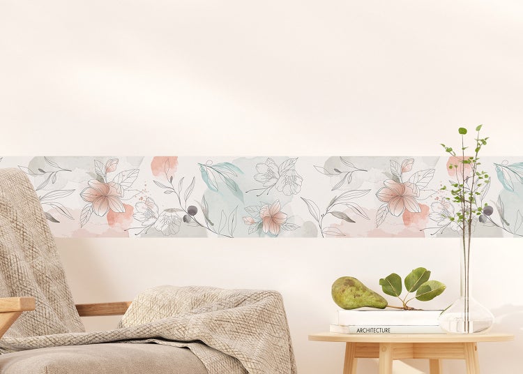 Tapetenbordüre mit floralem Aquarell-Muster an einer hellen Wand hinter einem Sessel und einem kleinen Holztisch.