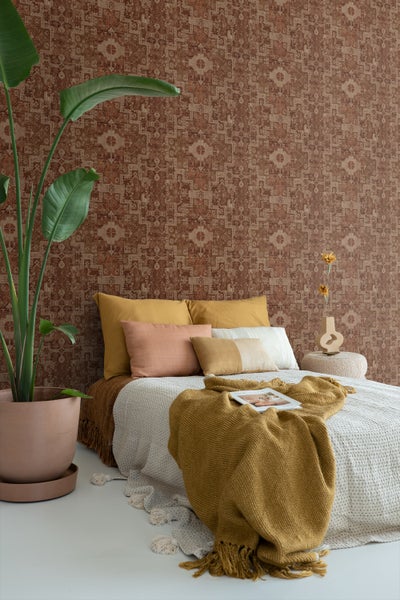 Dekoratives Schlafzimmer mit gemusterter Tapete, Kissen, Decken und Zimmerpflanze für ein gemütliches Ambiente.