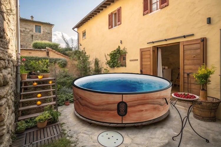 Runder Whirlpool mit Verkleidung in Holzoptik auf einer Steinterrasse in einem hellen, organisierten Innenhof mit Pflanzen.