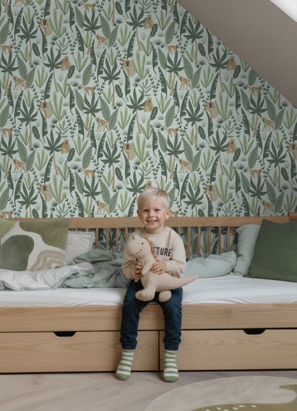 Vliestapete mit Dschungel-Motiv, Affen und tropischen Blättern in einem hellen Kinderzimmer mit Holzbett.