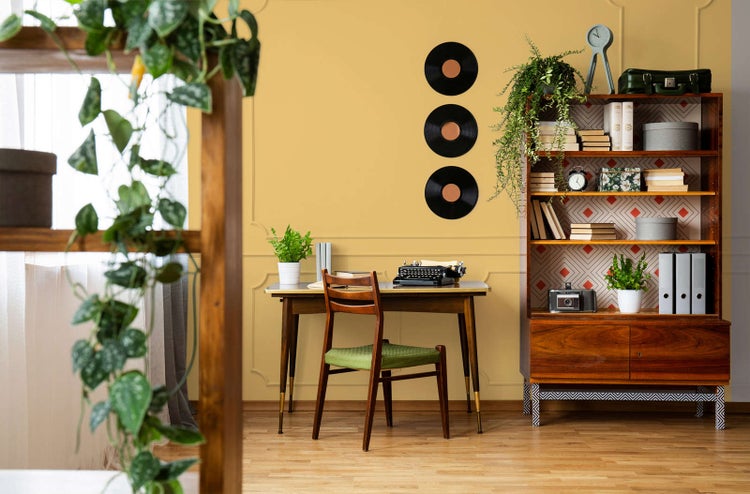 Helles Arbeitszimmer im Vintage-Stil mit Holzschreibtisch, Schreibmaschine, Holzregal und an der Wand befestigten Schallplatten.