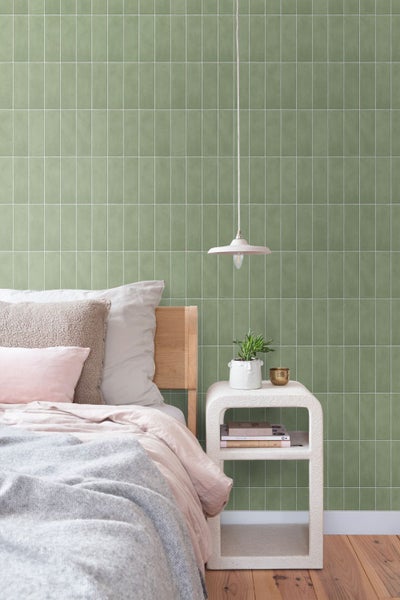 Schlafzimmer mit Wand in Fliesenoptik, hölzernem Bettgestell, beigefarbener Nachtkonsole und einer Pendelleuchte vor einer modernen Wohnraumwand