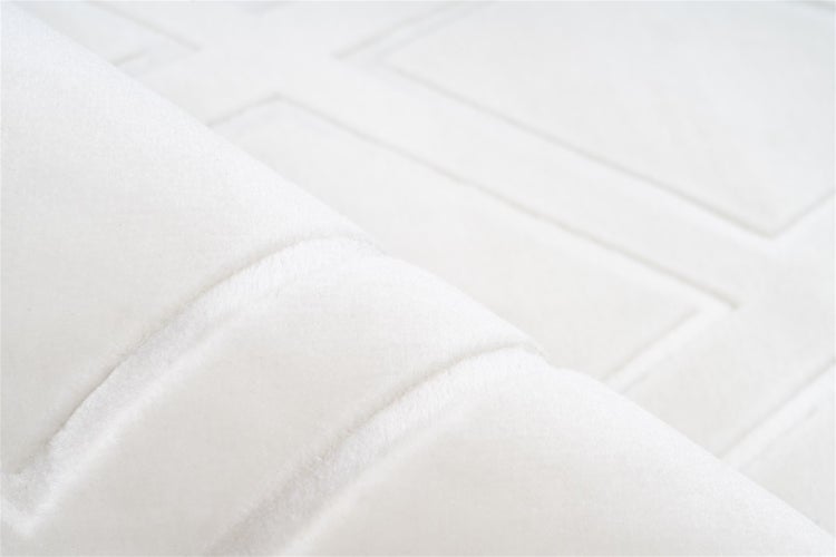 Nahaufnahme eines hellen Teppichs mit geometrischem Karomuster und umgeklappter Ecke, die die dunkle rutschhemmende Rückseite zeigt.