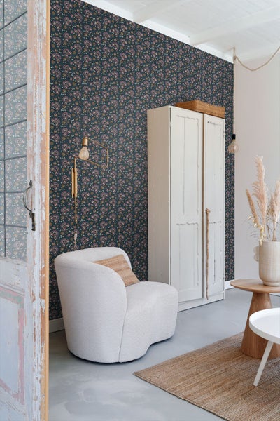 Wohnzimmer mit floral gemusterter Tapete, Sessel und Schrank