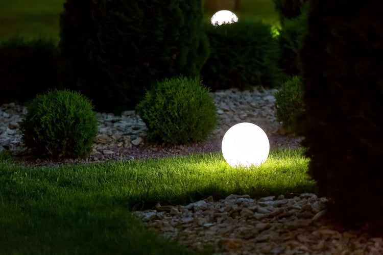 Szene mit Gartenbeleuchtung in Kugelform zwischen Rasen und Büschen