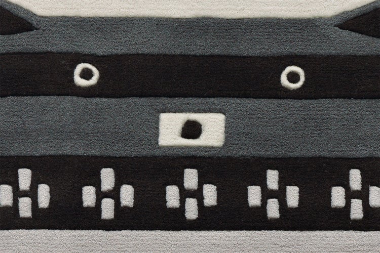 Detailansicht eines Teppichs mit geometrischem Muster, Streifen und verschiedenen Strukturen in Schwarz und Grau.