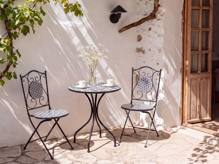 Bistroset bestehend aus einem runden Tisch und zwei Klappstühlen mit Mosaikmuster vor einer weißen Hauswand auf einer Steinterrasse.