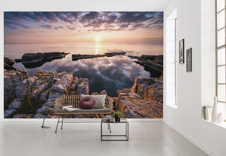 Wandbild mit Felsküste und Sonnenuntergang über dem Meer in einem hellen Raum.