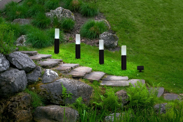 Szene mit mehreren Aussenleuchten entlang eines Steintreppenpfads in einem Garten.