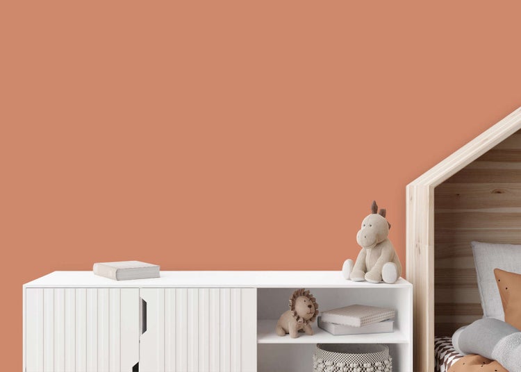 Wandfarbe in Terracotta im Kinderzimmer hinter einem weißen Sideboard mit Spielzeug und einem hölzernen Hausbett.