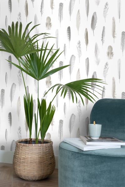Szene mit Zimmerpflanze in einem Korb, einem Samthocker, Büchern, einer Kerze und einer Tapete mit Federmuster.