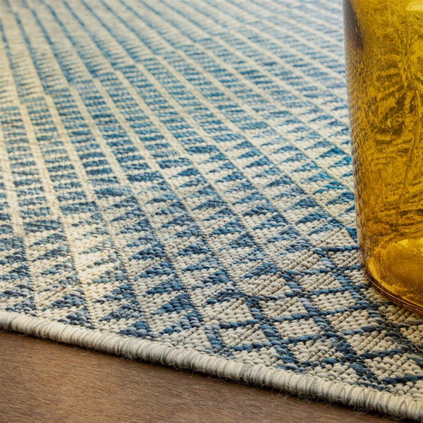 Detailansicht eines Flachgewebe-Teppichs mit blau-beigem geometrischem Muster auf einem Holzfußboden.