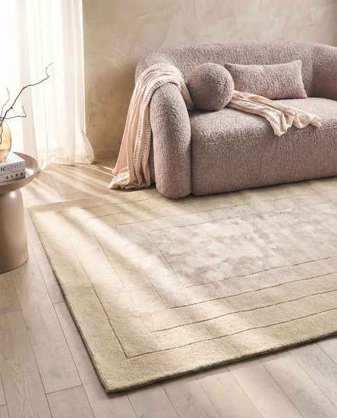 Großer rechteckiger Hochflor-Teppich mit strukturiertem Rahmen-Design in einem hellen Wohnzimmer mit Bouclé-Sofa und Holzfußboden.