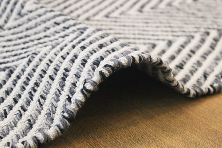 Nahaufnahme eines gewebten Teppichs mit einem geometrischen Muster aus diagonalen Linien und sichtbarer Webstruktur.