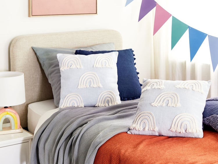 Dekoratives Kinderzimmer mit Bett, Kissen mit Regenbogenmuster und farbenfroher Wimpelkette