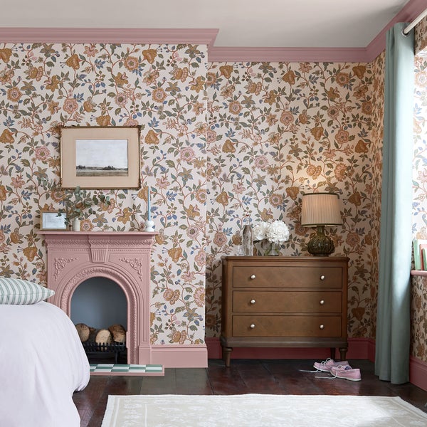 Klassisch eingerichtetes Schlafzimmer mit geblümter Tapete, einem dekorativen Kamin, einer Holzkommode und dunklem Holzboden.