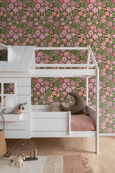 Kinderzimmer mit floraler Tapete mit rosa Blüten auf grünem Grund, einem Holzbett mit Baldachin und einem passenden Nachttisch.