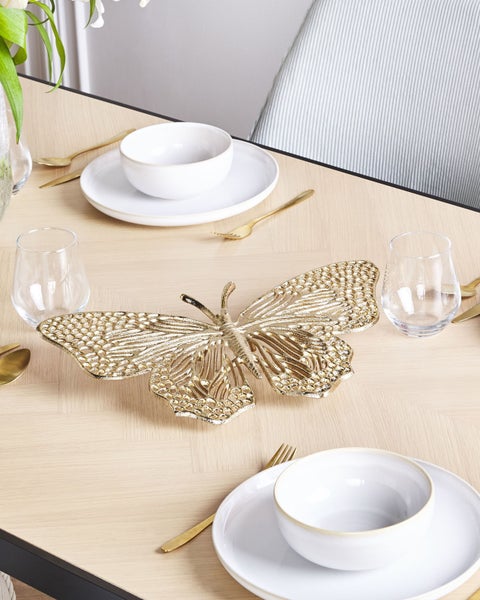 Tischdekoration mit goldener Schmetterlingsfigur, Geschirr und Gläsern auf einem Tisch