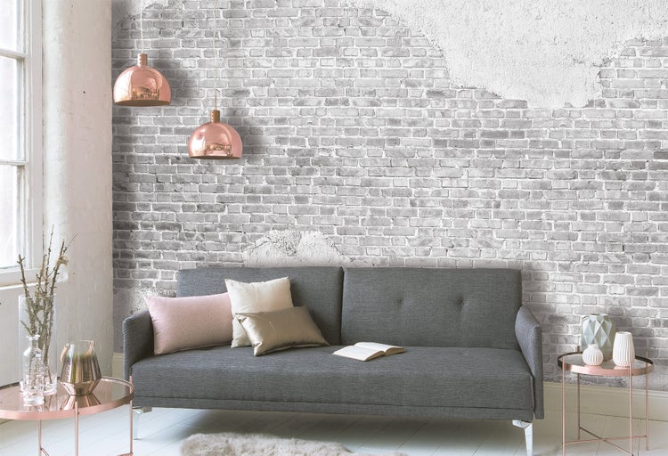 Fototapete mit Ziegelmauer-Optik und Putz-Elementen in einem modernen Wohnzimmer mit grauem Sofa und kupferfarbenen Hängelampen.