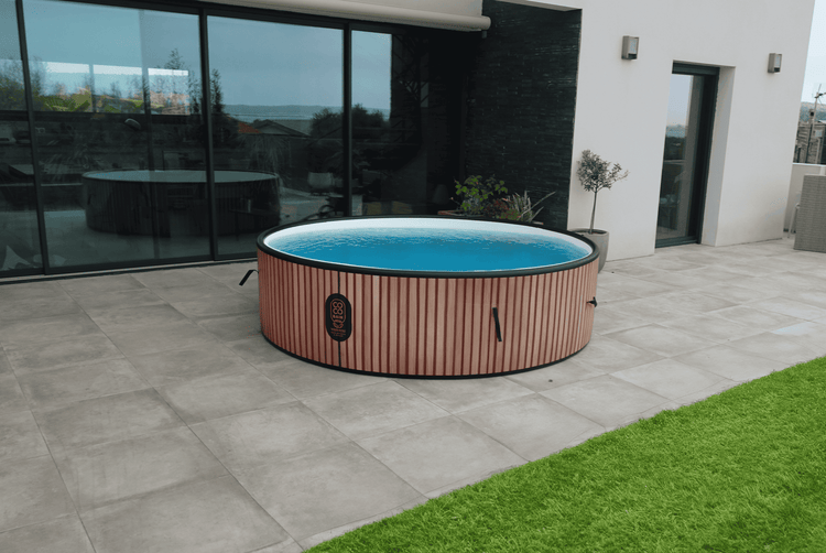 Runder Whirlpool mit Verkleidung in Holzoptik auf einer modernen Fliesenterrasse vor einer großen Glasfront.
