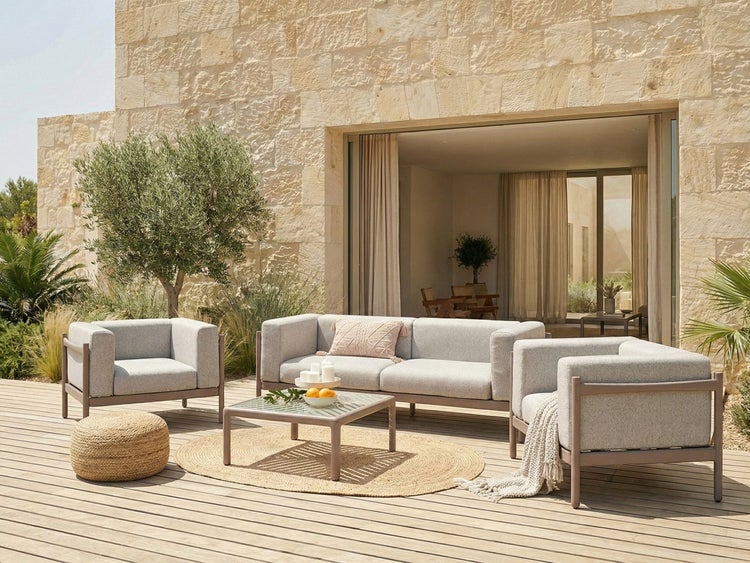 Moderne Outdoor-Lounge-Gruppe mit Sofa, zwei Sesseln und Couchtisch auf einer Holzterrasse vor einer hellen Natursteinwand.