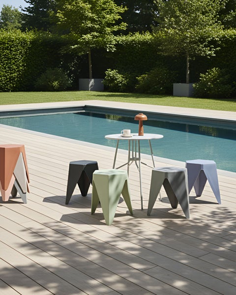 Moderner Außenbereich mit Pool, rundem Bistrotisch und verschiedenen geometrischen Hockern auf einer Terrasse in Holzoptik.