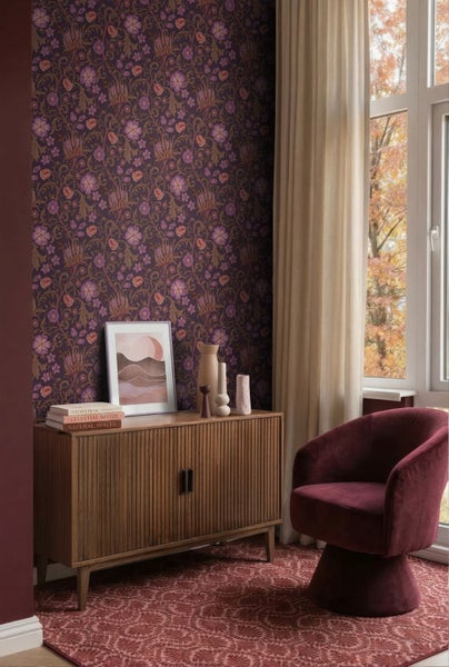 Tapete mit floralem Muster in einem Wohnzimmer mit Sideboard aus Holz, Samtsessel, Vasen, Büchern und Fenster mit Vorhängen.