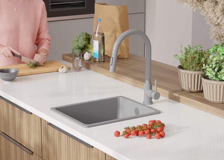 Küchenspüle mit Armatur, umgeben von Gemüse und Kräutern auf einer Arbeitsfläche.