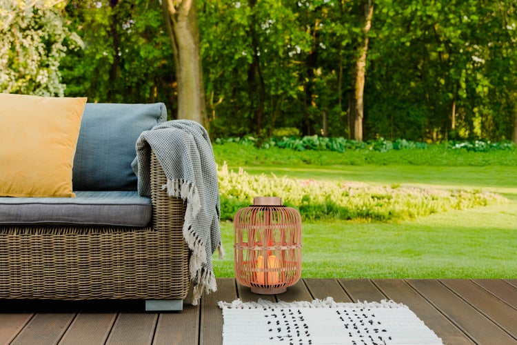 Szene mit Outdoor-Sofa, Kissen, Decke, Dekolaterne und Teppich auf einer Terrasse