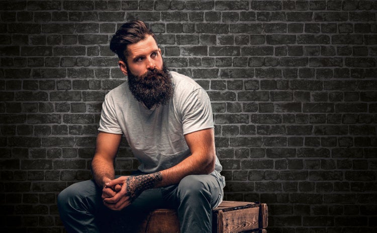 Mann mit Bart sitzt vor einer Ziegelwand